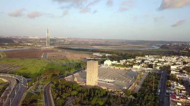 Panoramic aerial shot showcasing the historical Hassan Tower and Mausoleum in the foreground, with the futuristic VI Tower skyscraper visible on the horizon of Rabat-Sal&eacute; valley.