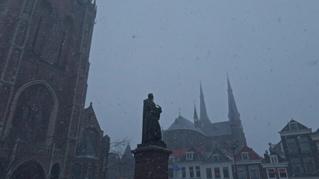 winter snowfall snow falling in the Netherlands in a Dutch city town in Europe with traditional architecture buildings and statue of European style, grey cloudy weather and ambient exterior calm vibe