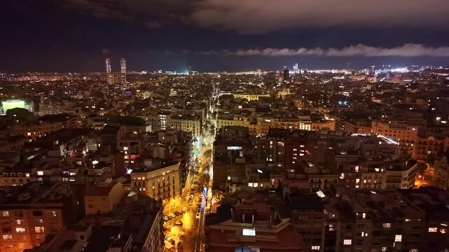 High night aerial view of Barcelona showing Gran Via de les Corts Catalanes cutting through the Eixample grid, and the vast metropolitan fabric extending toward the Collserola hills.