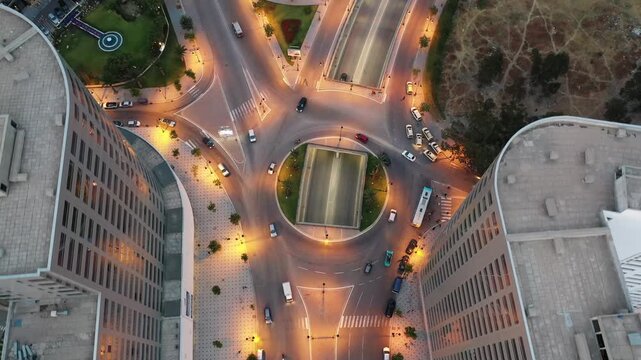 Aerial top-down drone shot of a busy urban intersection in Tangier at night. Features illuminated street lights, flowing vehicle traffic entering an underpass, and modern city architecture.