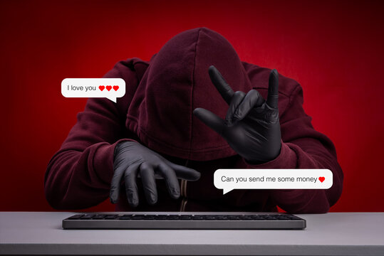 Hacker in hoodie and gloves using online romance scam tactics, sending fake love messages to deceive victims for money with I love You hand sign. Cyber fraud, romance scam, online deception concept.