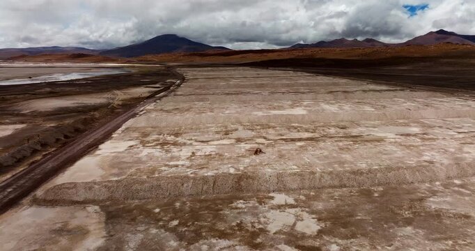 Borax extraction fields cover Laguna Capina salt lake in Potosi, Bolivia under storm clouds, wide forward drone shot.