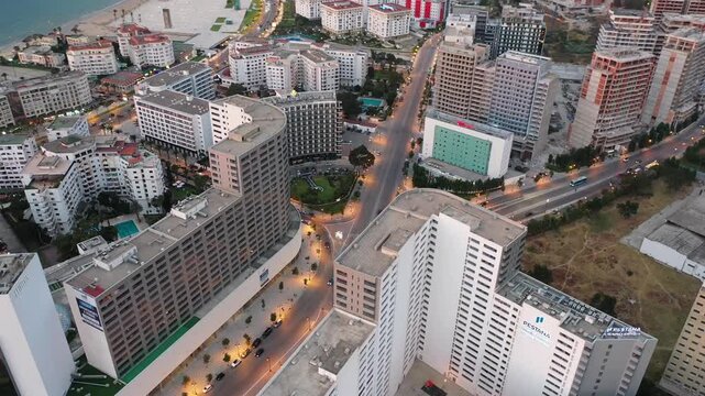 Aerial drone shot capturing the modern architecture of Tangier City Center at twilight. Features the Pestana Hotel, lit avenues, and high-rise commercial buildings in Northern Morocco.