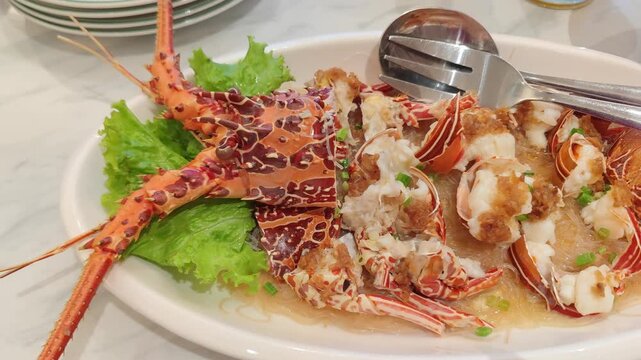 Video highlights a beautifully plated spiny lobster served on a bed of fresh green lettuce. The lobster is split open to reveal tender white meat, delicately garnished with savory sauce. Its vibrant o
