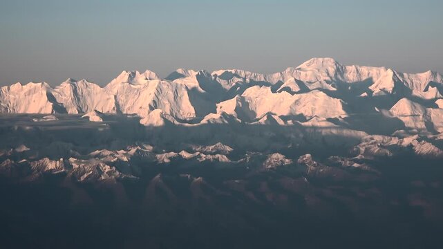 Aerial view of snow covered Pamir mountains with Ismoil Somoni Peak at sunrise light. High altitude panorama shows Hindu Kush and Tian Shan ridgelines, icy summits glowing above dark valleys.