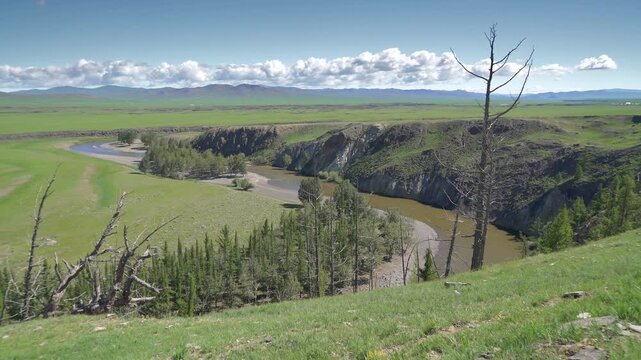 Panoramic river canyon landscape in Mongolia, rocky walls above winding water channel. Wide vista shows lush grasslands, stone cliffs, curving stream through basin, distant ranges.