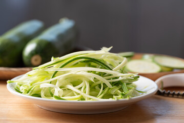 Fresh zucchini noodles (zoodles) in a white plate, prepared for healthy cooking