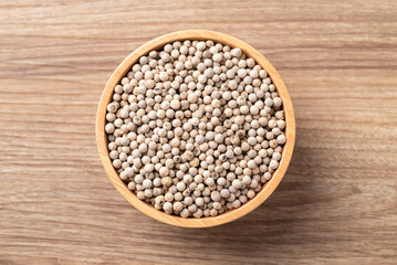 Fototapeta premium Top view of white peppercorns in a wooden bowl on wooden background, essential spices and seasoning for cooking