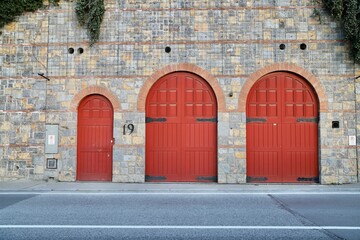 Historic Building Facade with Red Arched Doors, Vintage Wooden Warehouse Doors on Stone Wall