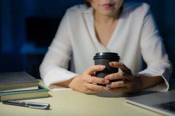 Fototapeta premium Businesswoman working late at night at her desk with holding a takeaway coffee cup