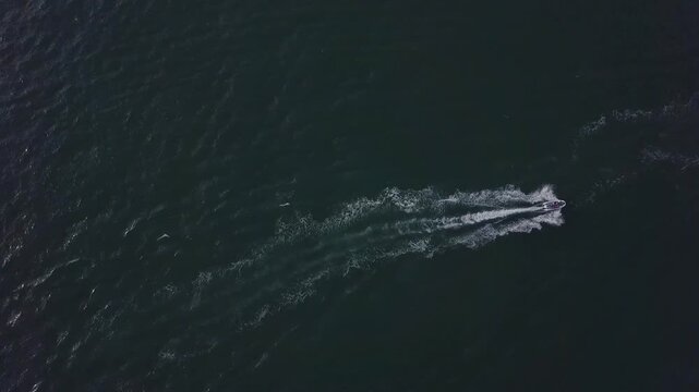 Top down aerial view of single jet ski creating white wake on deep blue ocean in Phu Quoc, Vietnam. Minimal tropical seascape symbolizing freedom and adventure travel.