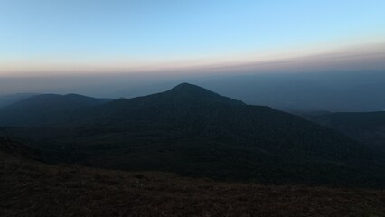 Atmospheric mountain layers at dawn with soft haze and pastel sky, tranquil landscape scenery.