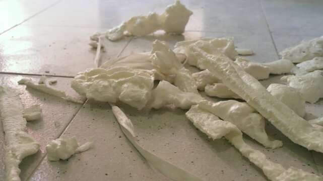 Hardened polyurethane foam pieces and construction waste lying on a dirty tiled workshop floor