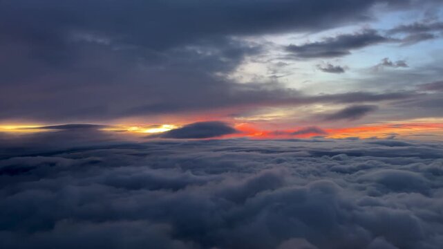 An aerial sunrise cloudscape taken from the cockpit of an airplane flying over an endless sea of stratus clouds and a golden horizon with the still hiden sun under the clouds.