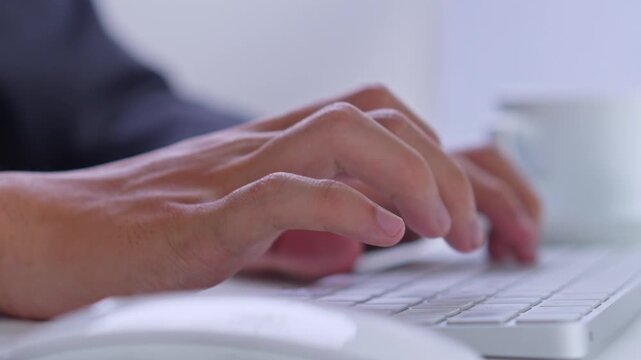 Side angle of businessman hands typing on wireless keyboard at professional desk with coffee cup