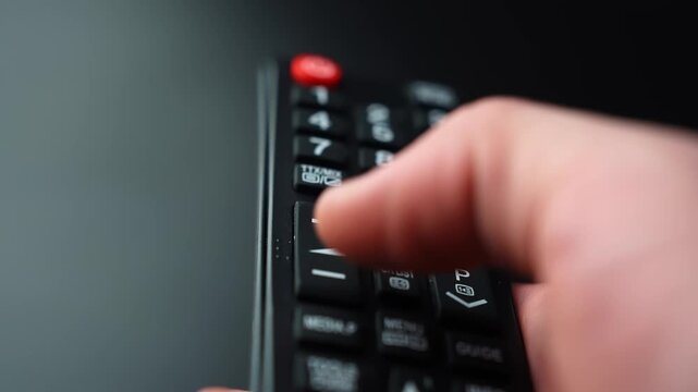 Close-up of a hand pressing the volume down button on a TV remote control, lowering sound level with shallow depth of field for home entertainment and audio control b-roll.