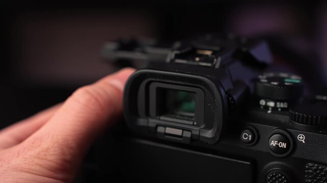 Slow rotation close-up of mirrorless camera electronic viewfinder and top controls, with hand support and soft studio bokeh for cinematic creator gear footage.