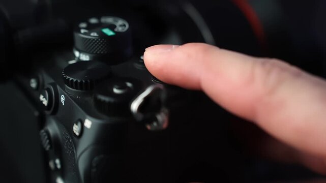 Finger presses the red record button on a mirrorless camera top plate, starting video capture in moody studio lighting with soft bokeh and shallow depth of field.