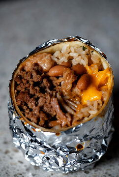 Delicious grilled chicken and vegetable burrito cut open on rustic table with melted cheese and fresh ingredients