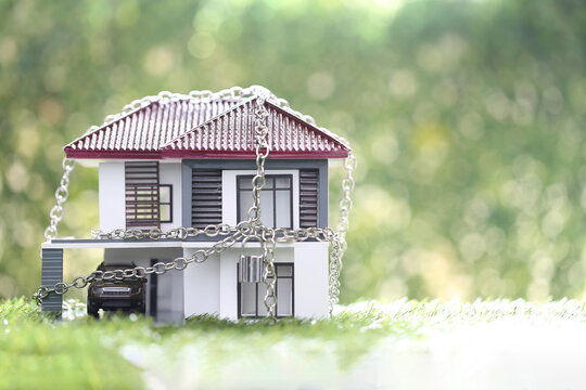 Model house locked with silver chain and padlock on green grass. Concept for home security, property seizure, foreclosure, real estate insurance, debt crisis and legal protection.