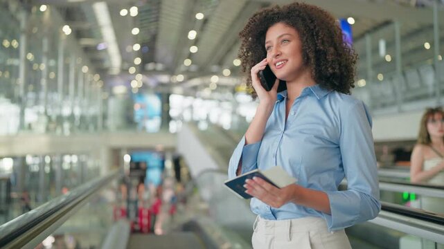 Latino woman talking on phone while walking through airport terminal. 