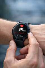 Fototapeta premium A person wearing a smartwatch displaying heart rate data on the screen while running outdoors during a sport activity using finger touch on the technology with their hand