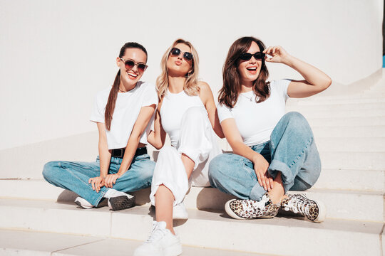 Three young beautiful smiling hipster female in trendy summer white t-shirt  and jeans clothes. Sexy carefree women posing in street. Positive models having fun, going crazy. In sunny day, sunglasses