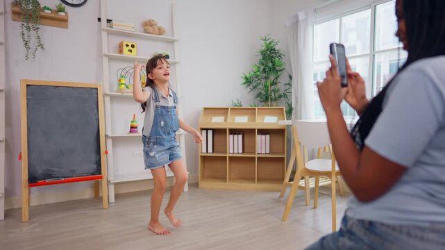 African teacher use phone record young child dancing in learning space. 