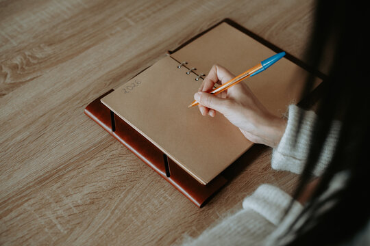 Une femme &eacute;crivant &agrave; la main dans un carnet artisanal sur une table en bois