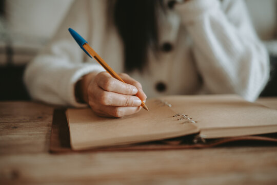 Une femme &eacute;crivant &agrave; la main dans un carnet artisanal sur une table en bois