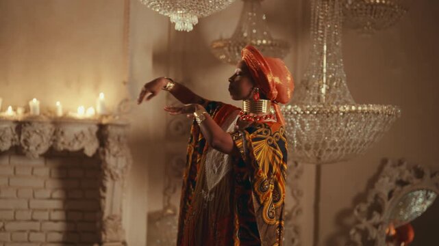 Enigmatic dance of pretty african woman in ethnic gown in darkness, save culture . Traditions and heritage of africa, beautiful black lady in traditional dress and turban dancing in royal palace