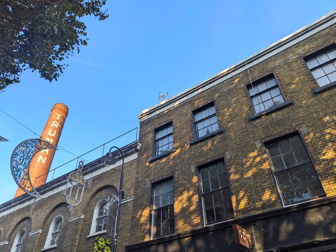 The iconic Truman Brewery chimney and historic brick facade on Brick Lane under a clear blue sky