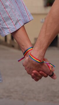 Closeup of a gay couple walking hand in hand through the city streets. They are wearing matching lgbt rainbow pride flag bracelets
