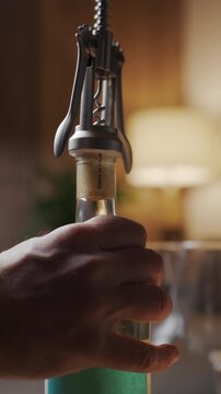 Close-up of hand using corkscrew to open white wine bottle in home interior. Concept of alcohol drink preparation and evening relaxation