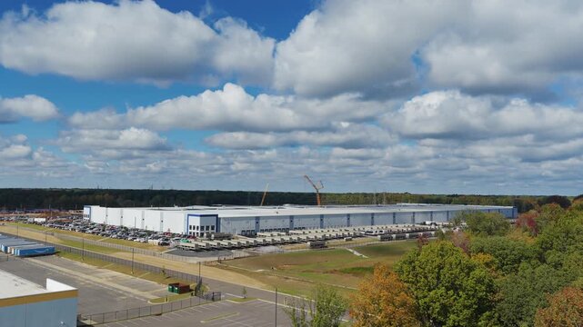 Wide drone dolly forward tilt down over fall trees revealing data facility in Southaven Mississippi United States