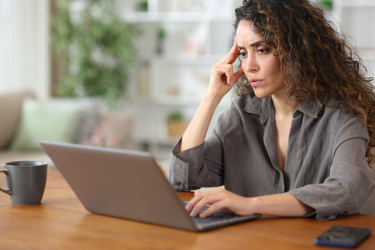 Worried adult woman at home checking bad news on laptop