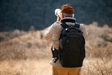 Rear view of backpacked senior photographer who explores open fields to capture a unique perspective of nature or wildlife.