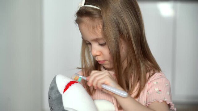 Little girl brushes teeth of toy shark with toothbrush. Oral hygiene. Health care