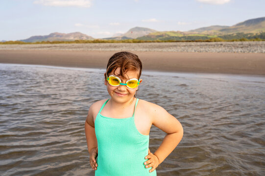 Smiling girl in swimming goggles looking at camera in shallow sea.