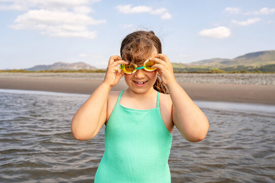 Child girl adjusting swimming goggles in calm shallow wate