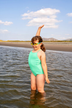 Joyful child girl raising hand ready to swim in the sea.