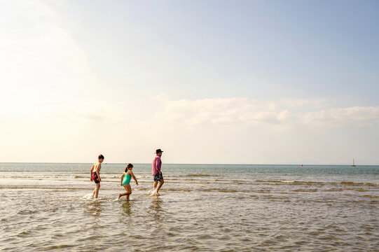 Single father walking with two children through shallow sea.