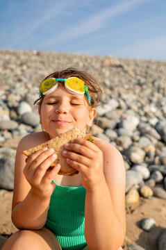 Smiling girl eating sandwich on sandy beach.
