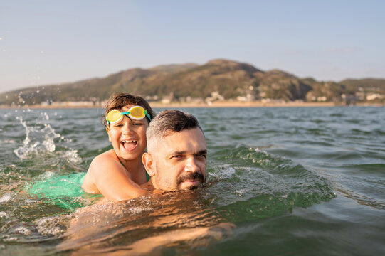 Father carrying daughter on his back while swimming in sea.