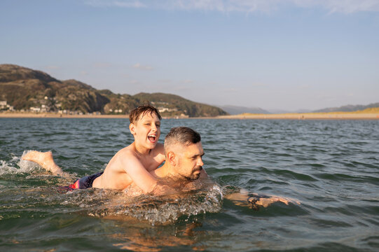 Father swimming with son on his back in sea.