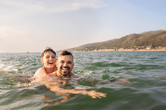 Teenage boy riding on father back in sea.