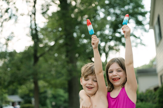 Two kids holding red white blue popsicles outdoors