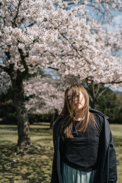 Young woman in black coat enjoying cherry blossoms in spring par