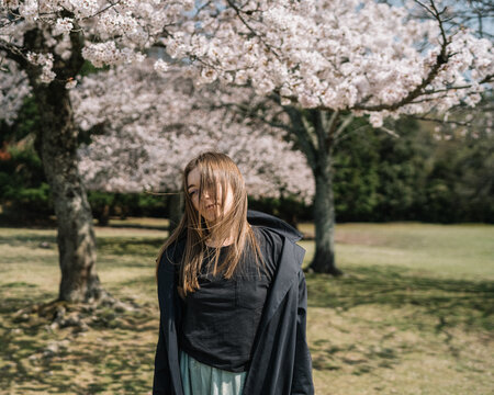 Young woman in black coat enjoying cherry blossoms in spring par