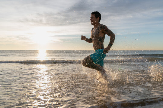 Athletic man running splashing water on ocean beach
